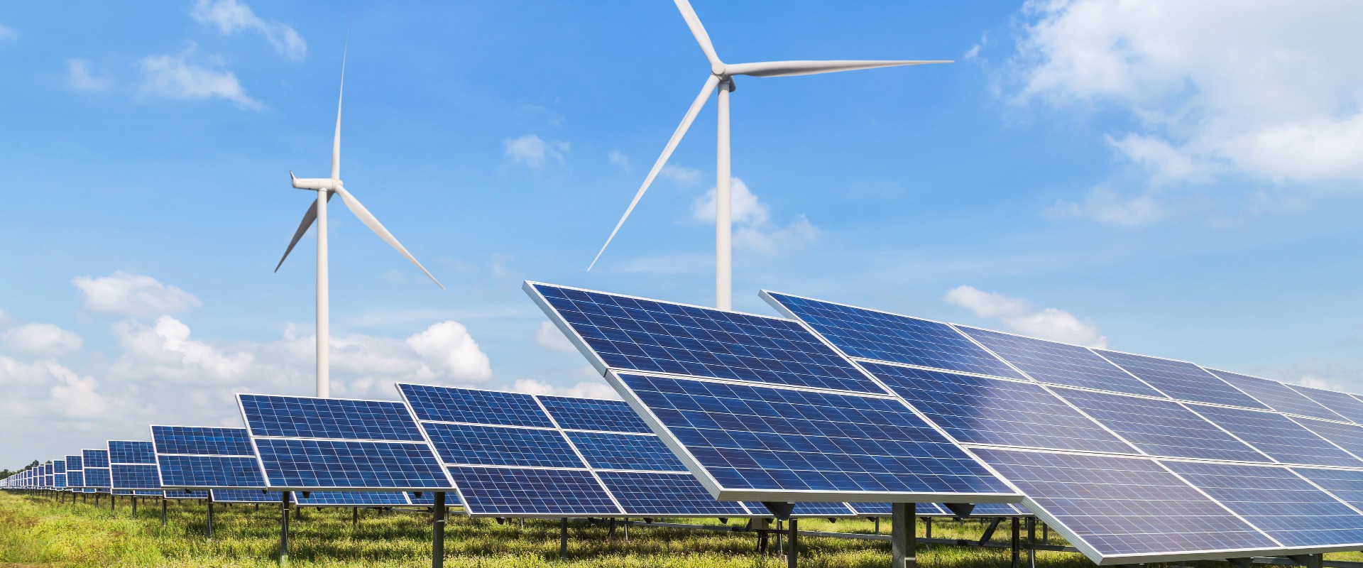 Feld mit vielen Solaranlagen und einem Windrad im Hintergrund